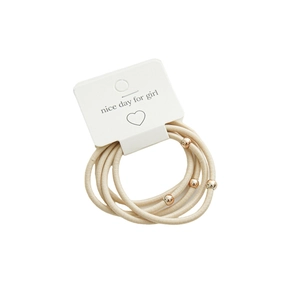 Five minimalist beige elastic hair ties with gold bead accents on a display card