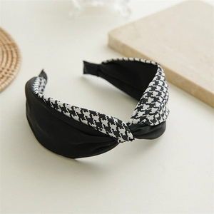 Detailed view of elegant houndstooth and black fabric knotted headband on a beige surface