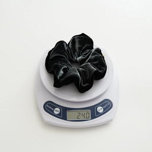 Detail view of a 24.0g heavy black velvet hair scrunchie weighed on a digital scale