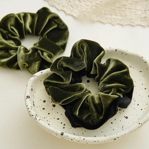 Close-up of two elegant dark olive green velvet scrunchies on a ceramic plate