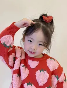 Detalle de jersey de punto rojo para niña con jacquard de fresas y pinza de pelo de corazón