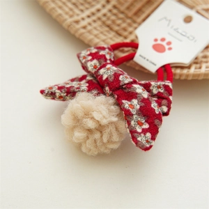 Detalle de goma de pelo con lazo floral rojo y pompón de peluche sobre tarjeta