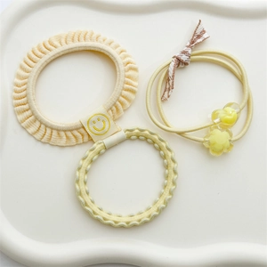 Three-piece set of pale yellow hair ties including scrunchie and floral charms on a tray