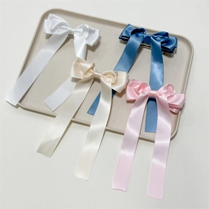 Detailed view of satin bow hair clips with long ribbons in four elegant colors on a tray