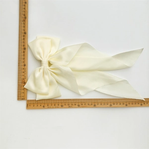 Dettaglio delle dimensioni del fiocco in raso crema con nastri e misura di 16 cm su righello