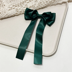 Detail view of smooth dark green satin bow hair clip with elegant long ribbons on a tray