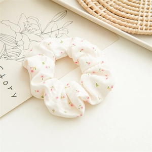Close-up of floral fabric scrunchie with pink flowers and green leaves on beige linen