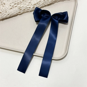 Detail of dark blue satin bow hair clip with long ribbons on a textured background