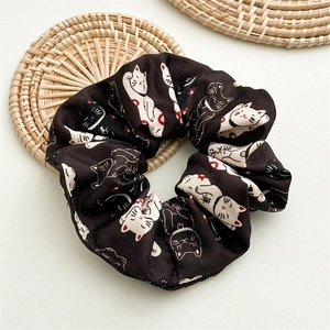 Détail d'un chouchou en tissu noir avec motif chat porte-bonheur sur fond rustique