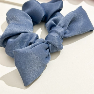 Close-up of a blue satin knotted scrunchie with elegant bow detail and silky texture
