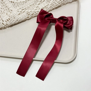 Detail of wine red satin hair bow clip with long ribbons on a cream vintage tray