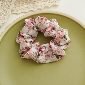 Dettaglio di scrunchie floreale con rose su un piatto di ceramica con pizzo