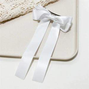 Detail of white satin three-layer bow hair clip with long streamers on beige tray