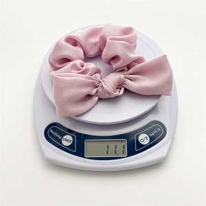 Detail shot of a light pink satin bow scrunchie showing 11.1g weight on a scale