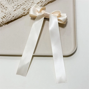 Detailed close-up of a creamy white triple-layer satin bow hair clip with long streamers