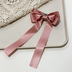Detail of pink satin three-layer bow hair clip with long ribbons on a beige tray