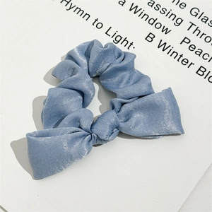 Detailed view of light blue satin scrunchie with smooth silk texture and bow knot