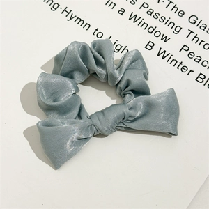Detail showing the glossy silk satin texture and bow design of the grey-blue scrunchie