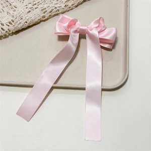 Detailed close-up of pink satin bow hair clip with long ribbons on a lace background