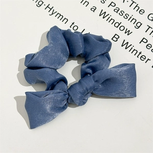 Detail of elegant dusty blue satin scrunchie with knot bow design on a white display
