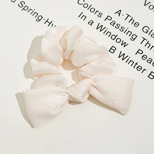 Detailed close-up of light pink satin scrunchie with soft pleats and knotted bow design