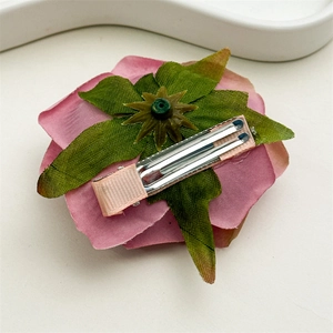 Detail view showing pink fabric rose hair clip with green leaves and a silk-wrapped metal grip