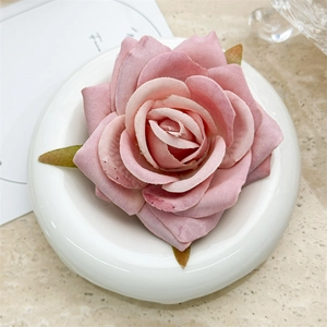 Close-up of a pink fabric rose hair clip with detailed petals and green leaves