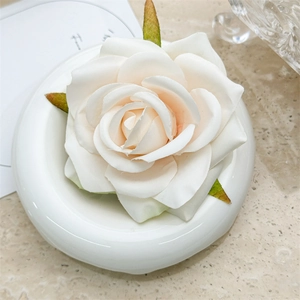 Detail of a creamy white silk rose hair clip with green leaves on a ceramic tray