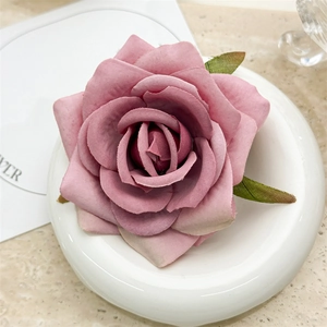 Macro detail of dusky pink fabric rose hair clip with green leaves on ceramic tray