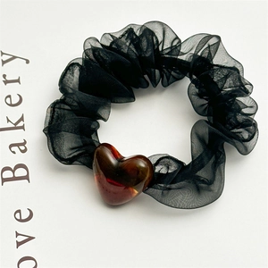 Detail of black mesh scrunchie with a glossy amber resin heart pendant for hair styling