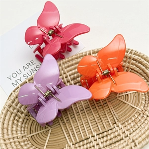 Trois pinces à cheveux papillon colorées en rose, orange et violet sur un plateau