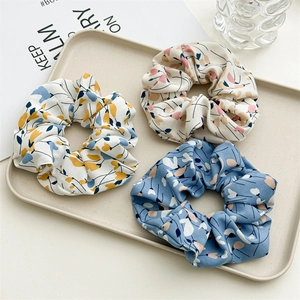 Detailed view of three floral fabric hair scrunchies displayed on a minimalist tray