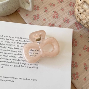 Detail of peach pink matte resin hair claw clip shaped like a bow on an open book page
