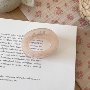 Detailed close-up of a pink resin geometric hair claw clip on vintage book and floral fabric