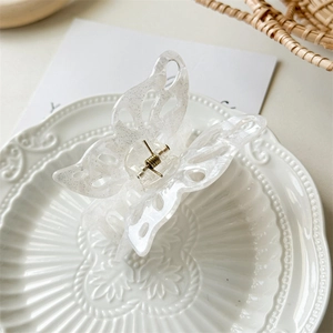 Detail of transparent glitter butterfly hair claw clip with hollow wings on white ceramic plate