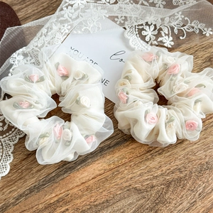 Close-up of white organza scrunchies with pink silk roses and green leaf details
