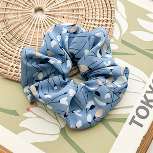 Detail of light blue floral chiffon scrunchie on woven mat with soft lighting