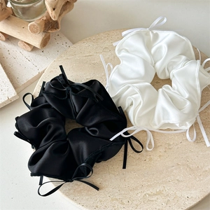 Détail de chouchous en satin noir et blanc avec nœuds délicats posés sur un plateau en pierre