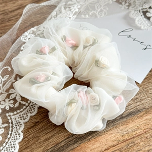 Detail of white mesh organza scrunchie with pink rose floral accents on wooden surface