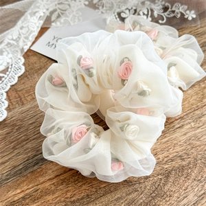 Close-up of white organza scrunchie with pink rose embroidery on wooden surface