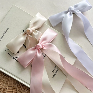 Détail de trois barrettes à longs rubans de satin en beige, rose et blanc élégant