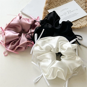 Trois chouchous en satin avec nœuds en rose, noir et blanc sur un tapis décoratif