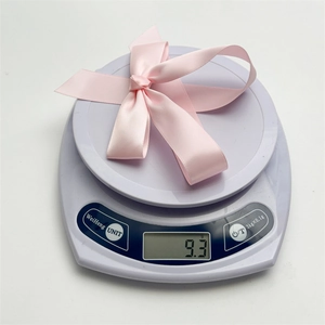 Détail d'un nœud papillon en satin rose sur une balance indiquant un poids de 9,3g