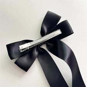 Elegante pinza para el pelo con lazo de satén negro y clip metálico sobre fondo blanco