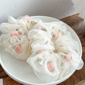 Detail of elegant cream mesh scrunchie with 3D ribbon roses and green leaves decoration