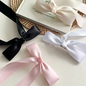 Barrettes à nœuds en satin noir, rose et blanc disposées sur un tapis de paille tressée