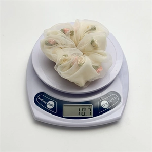 Detail view of cream organza hair scrunchie with rose floral accents weighing 10.7g