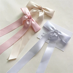 Détail de trois barrettes à nœuds en satin blanc, rose et beige avec de longs rubans