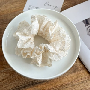 Detailaufnahme von cremefarbenem Spitzen-Haargummi mit Stickerei auf Keramikteller
