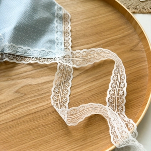 Détail d'un tissu à pois bleu clair avec bordure en dentelle blanche sur bois